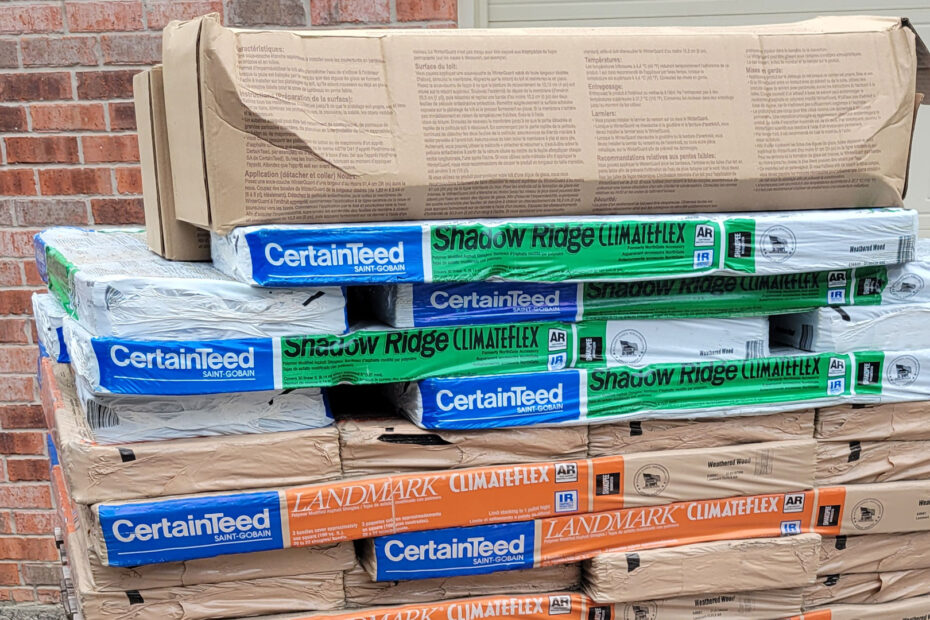 Piled-up shingles prior to be installed on a roof. Certainteed's ClimateFlex® - Colored in weathered wood. And Shadow Ridge® plus Solar Power Attic Vents installed in Tomball, Texas (a city between Cypress and Spring in Northern Houston).