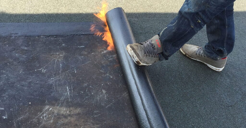 A construction worker applies asphalt membrane for flat roof modified bitumen